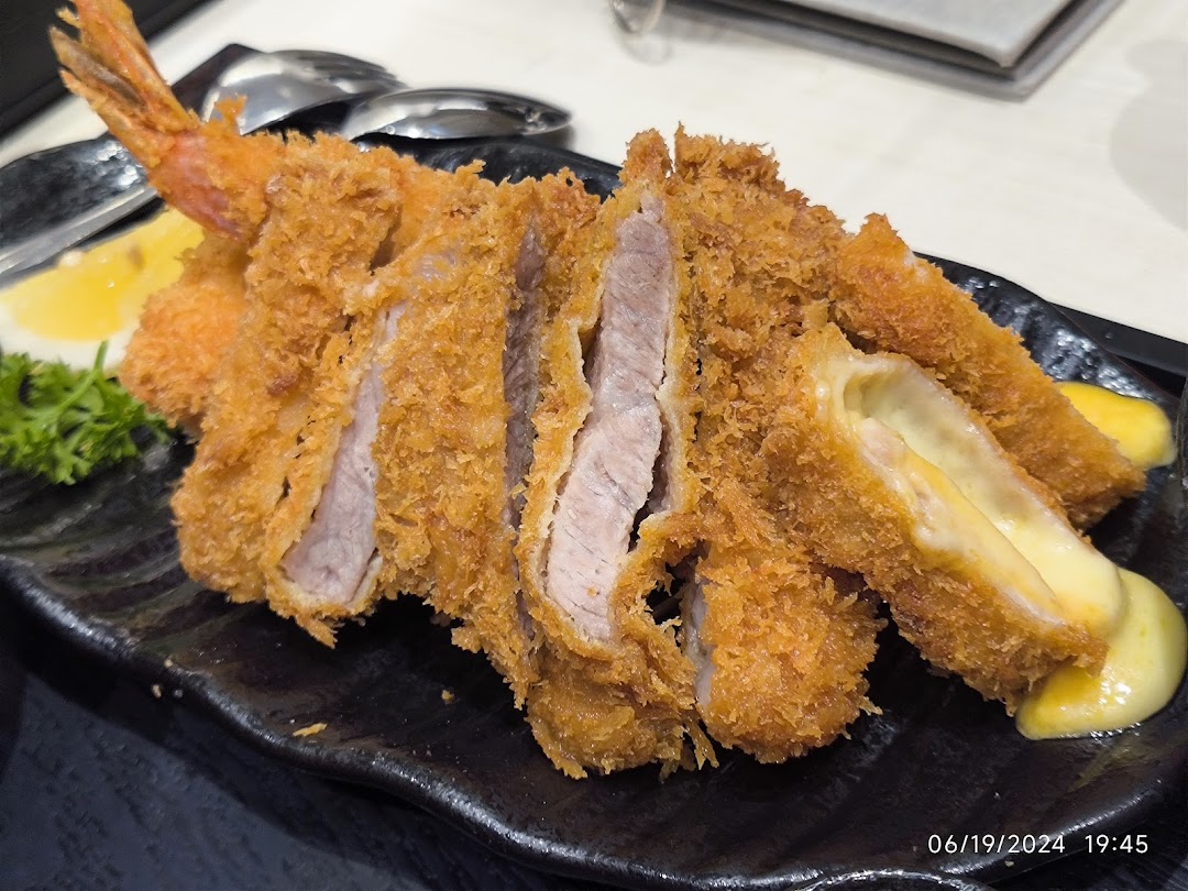 A close-up of crispy fried pork cutlets, shrimp, and cheese-filled katsu served on a black plate.