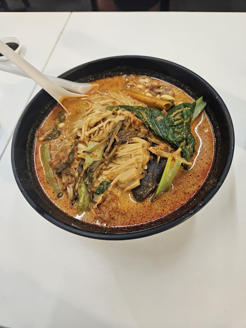 A vibrant bowl of spicy noodles with various vegetables and ingredients, served on a white table.