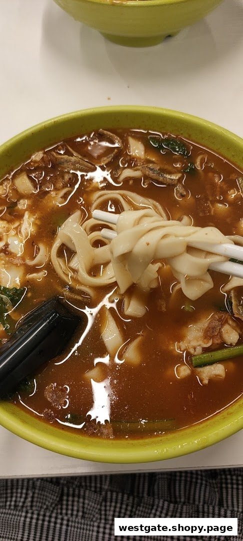 A close-up of a hearty bowl of noodles with rich broth, meat, and vegetables, held by chopsticks.