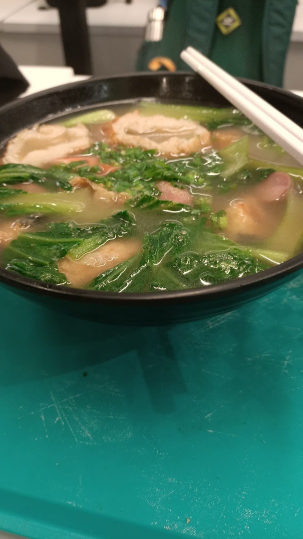 A close-up of a steaming bowl of soup or noodles with vegetables and meat, served with chopsticks.