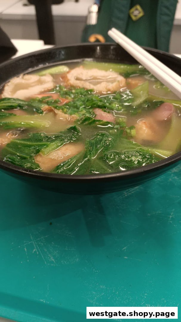 A close-up of a steaming bowl of soup or noodles with vegetables and meat, served with chopsticks.