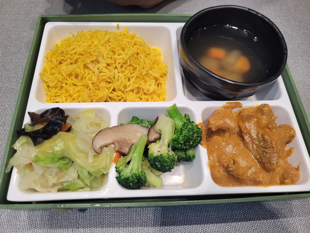 A vibrant bento-style meal featuring yellow rice, soup, mixed vegetables, and a rich curry dish.