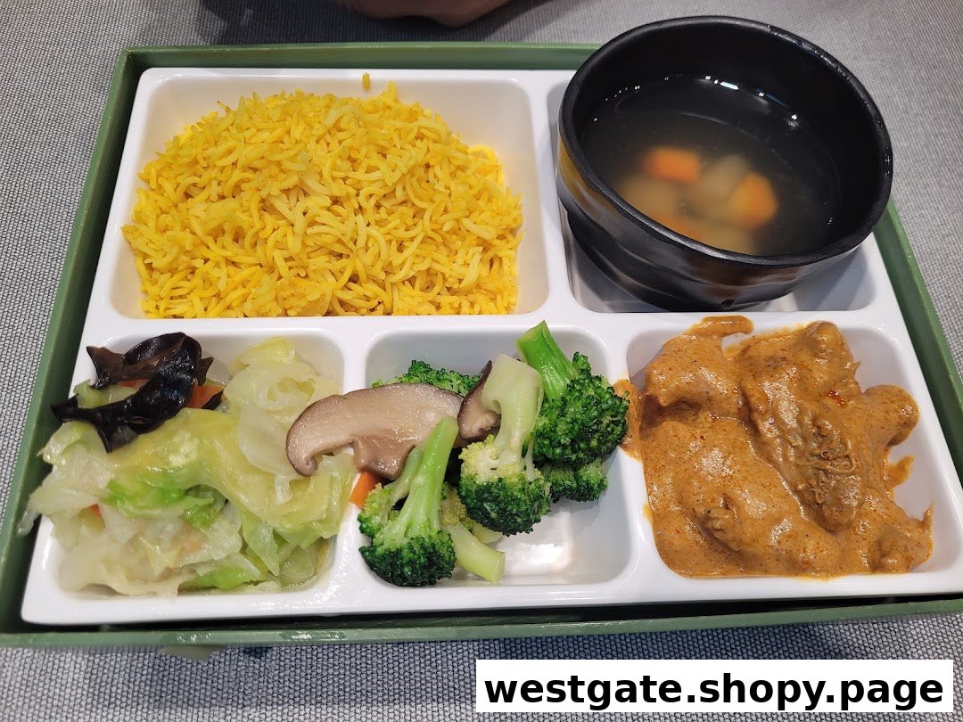 A vibrant bento-style meal featuring yellow rice, soup, mixed vegetables, and a rich curry dish.