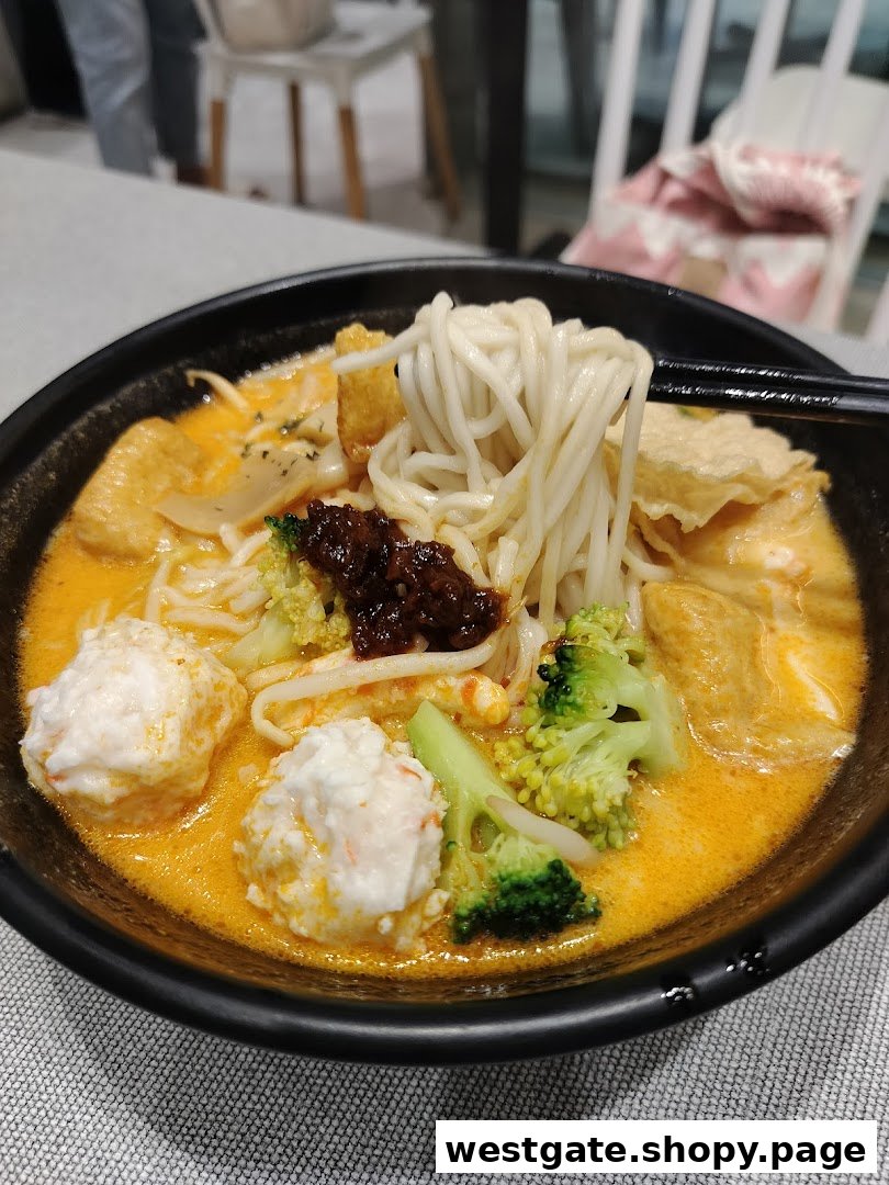 A close-up of a vibrant bowl of noodles with rich broth, fish balls, broccoli, and chili paste.