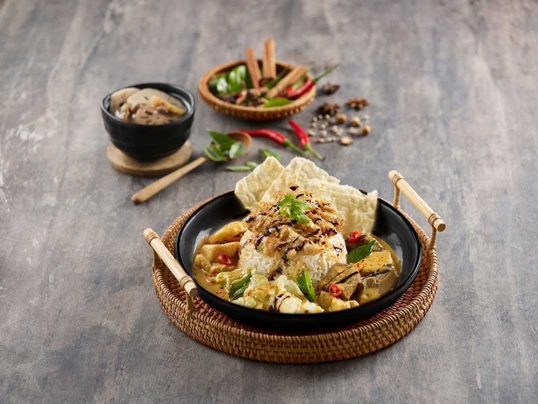 A vibrant plant-based curry dish with rice, crackers, and a side, artfully presented.