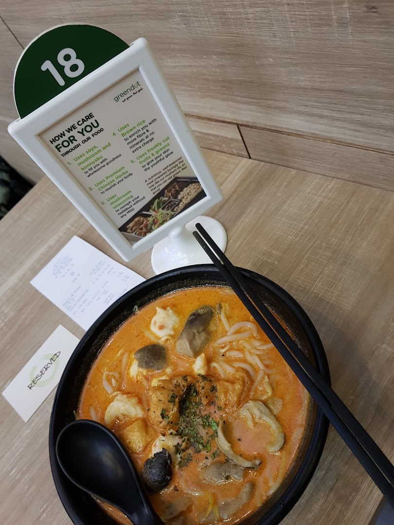 A vibrant bowl of laksa-style noodles with a table display explaining Greendot's healthy food philosophy.