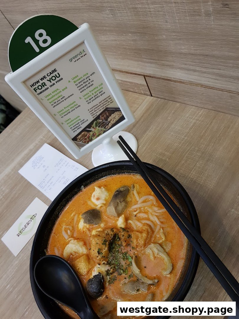 A vibrant bowl of laksa-style noodles with a table display explaining Greendot's healthy food philosophy.