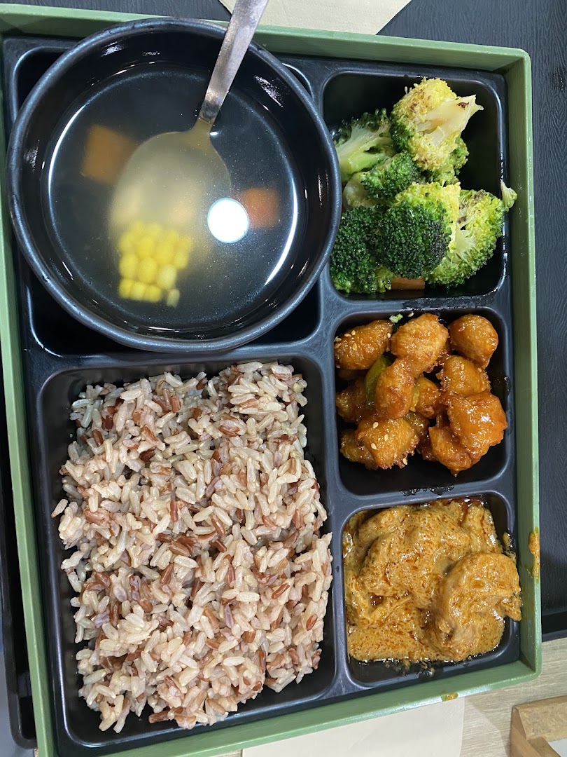 A healthy bento box meal featuring mixed grain rice, soup, broccoli, and two main dishes.