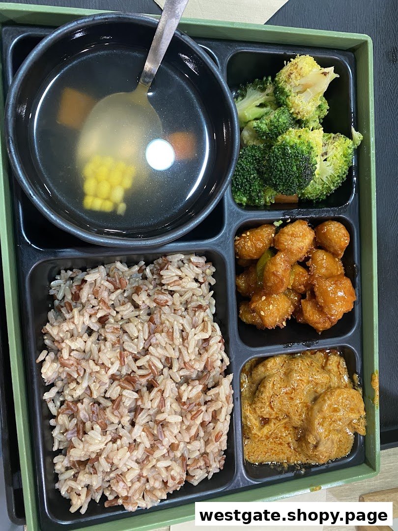 A healthy bento box meal featuring mixed grain rice, soup, broccoli, and two main dishes.