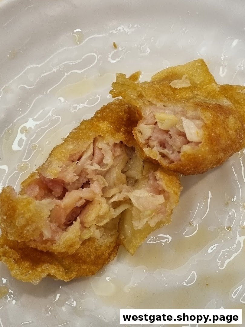 A close-up of a golden-fried dumpling, cut open to reveal its savory meat filling on a white plate.