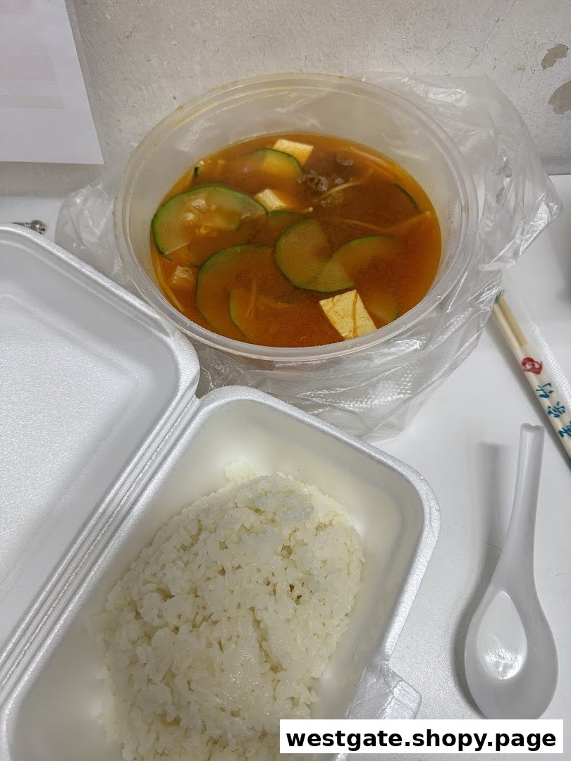 A delicious takeout meal featuring spicy soup with zucchini and tofu, served with white rice.