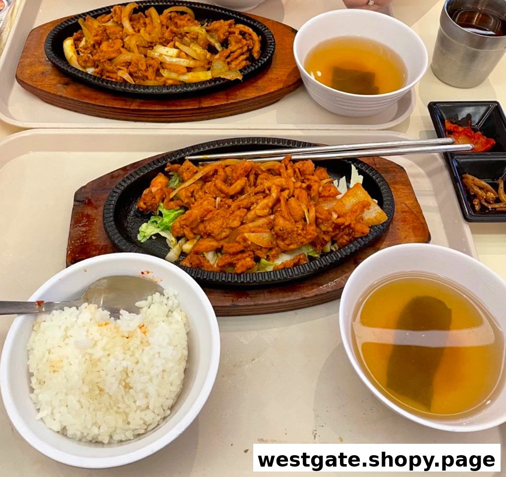 Two sizzling plates of spicy Korean chicken with rice, soup, and banchan, ready to be enjoyed.