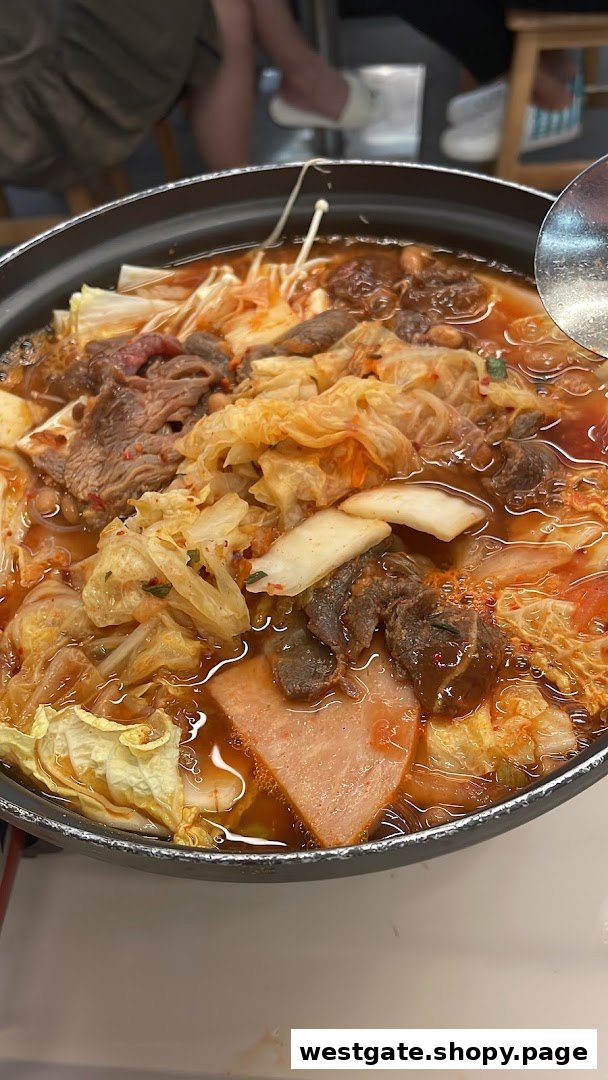 A bubbling pot of Korean budae jjigae (army stew) with various ingredients like meat, kimchi, and mushrooms.