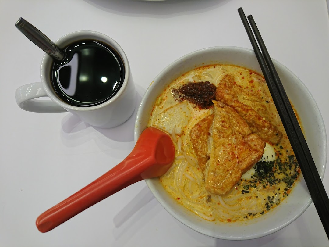 A vibrant bowl of Hainanese curry noodles or laksa served with a cup of traditional coffee.