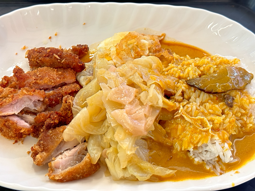 A close-up of Hainanese curry rice with crispy fried pork cutlet, braised cabbage, and a fried egg.