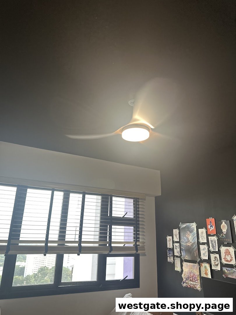 A modern ceiling fan illuminates a room with a large window and a wall adorned with various artworks.
