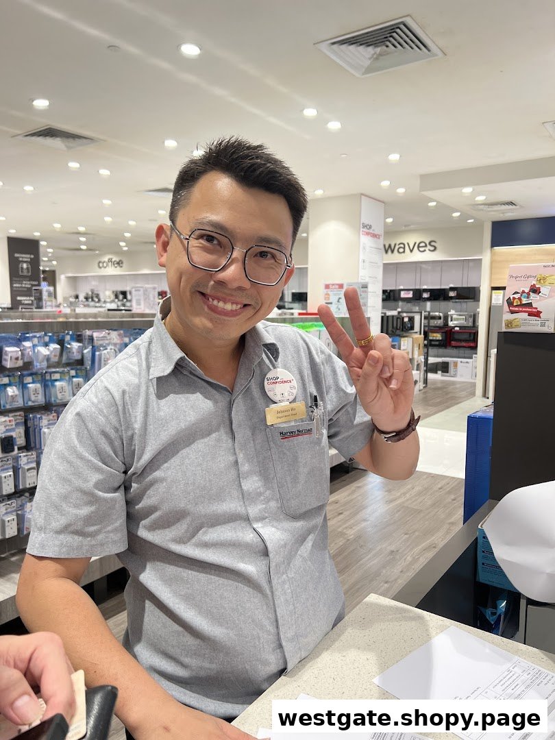 A friendly Harvey Norman staff member smiles and makes a peace sign inside the electronics and appliance store.