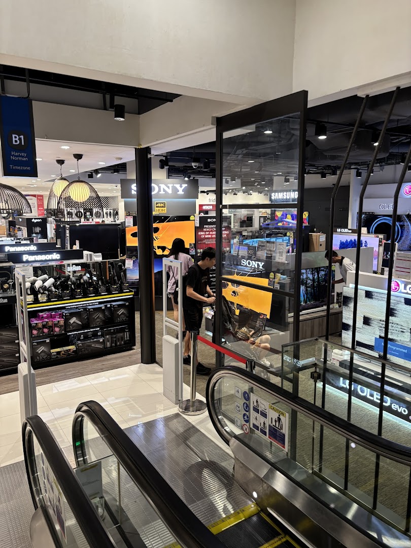 View from an escalator into Harvey Norman, showcasing electronics and home appliances.