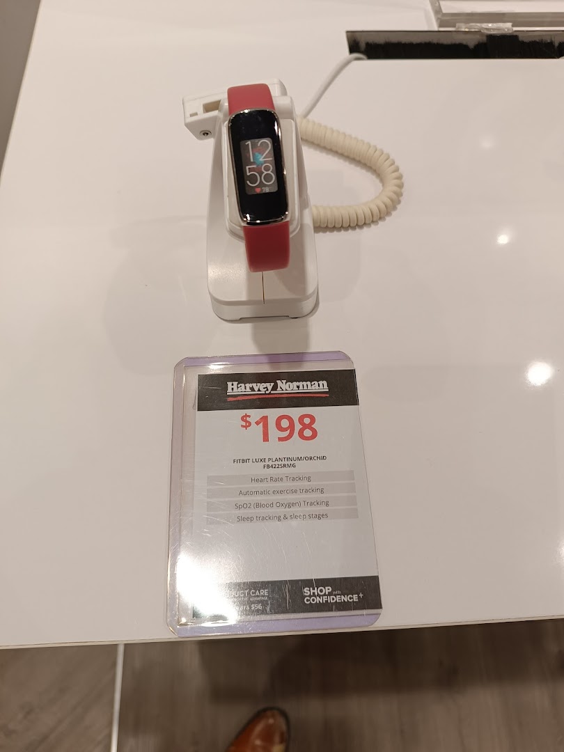 A red Fitbit Luxe fitness tracker displayed with its price and features at Harvey Norman.