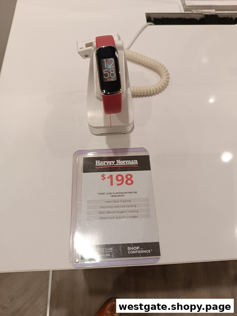 A red Fitbit Luxe fitness tracker displayed with its price and features at Harvey Norman.