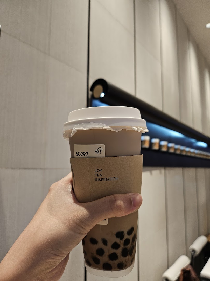 A hand holds a HEYTEA bubble tea with tapioca pearls, featuring a 'JOY TEA INSPIRATION' sleeve.
