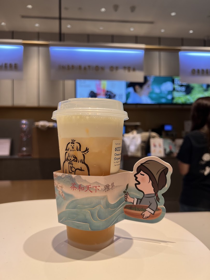 A HEYTEA cheese foam tea drink with a decorative sleeve on a counter inside the shop.