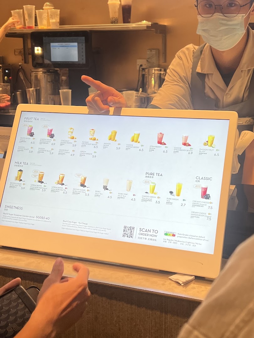 A customer views a digital menu screen at HEYTEA, displaying various fruit, milk, and pure tea options.