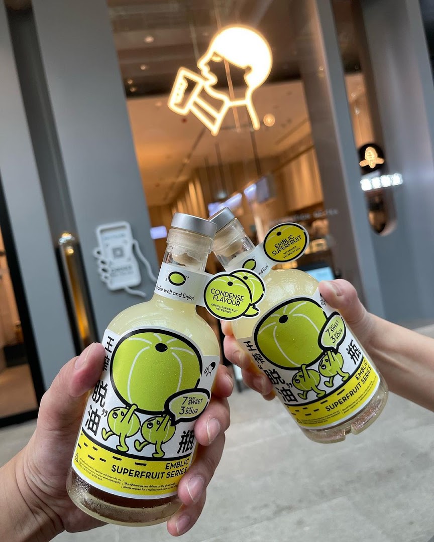 Two hands holding HEYTEA Emblic Superfruit Series bottled drinks with the shop interior in the background.