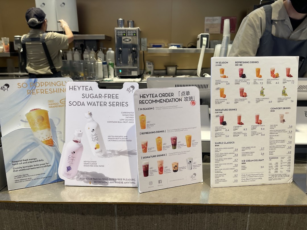 A counter view of HEYTEA with various drink menus, promotional displays, and staff preparing beverages.