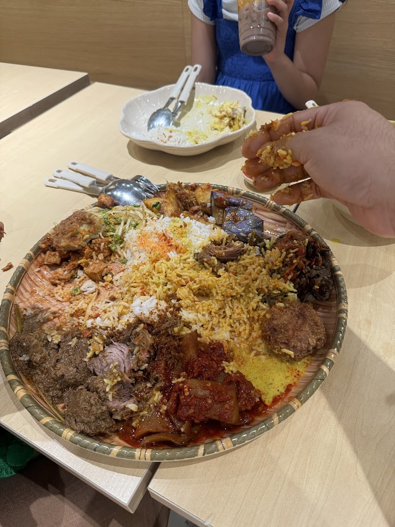 A large, vibrant platter of traditional Malay dishes, likely Nasi Ambeng, being enjoyed by diners.