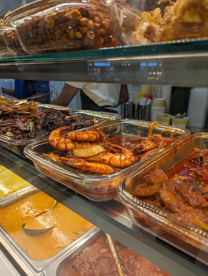 A vibrant display of traditional Malay dishes, including prawns and curries, in a food counter.