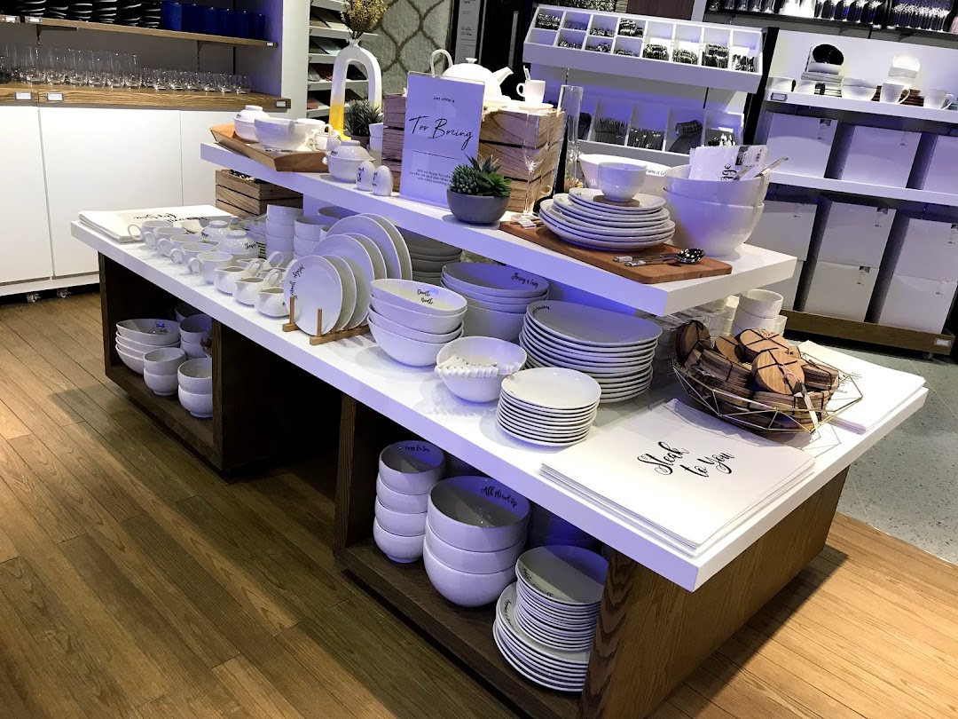 A display of elegant white dinnerware, bowls, and home accessories in a modern retail setting.