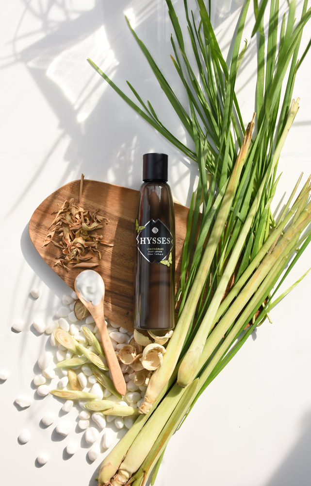 A HYSSES lemongrass product bottle displayed with fresh lemongrass, dried botanicals, and white stones.