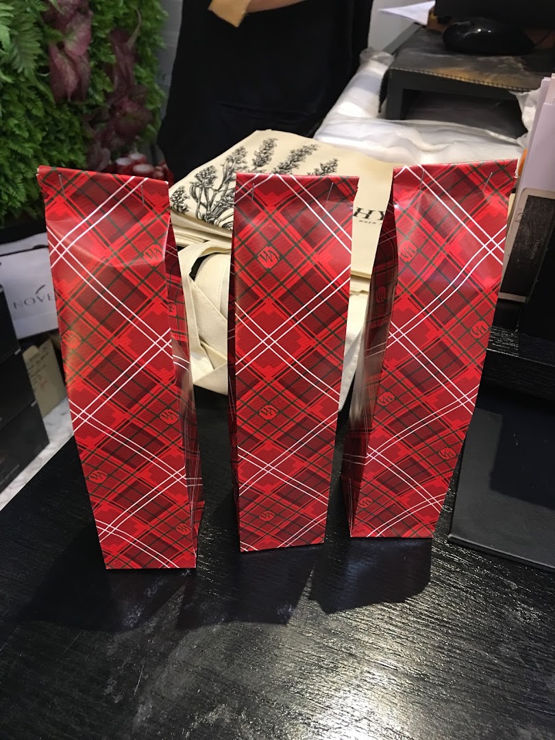 Three festive red plaid gift bags from HYSSES on a dark counter.