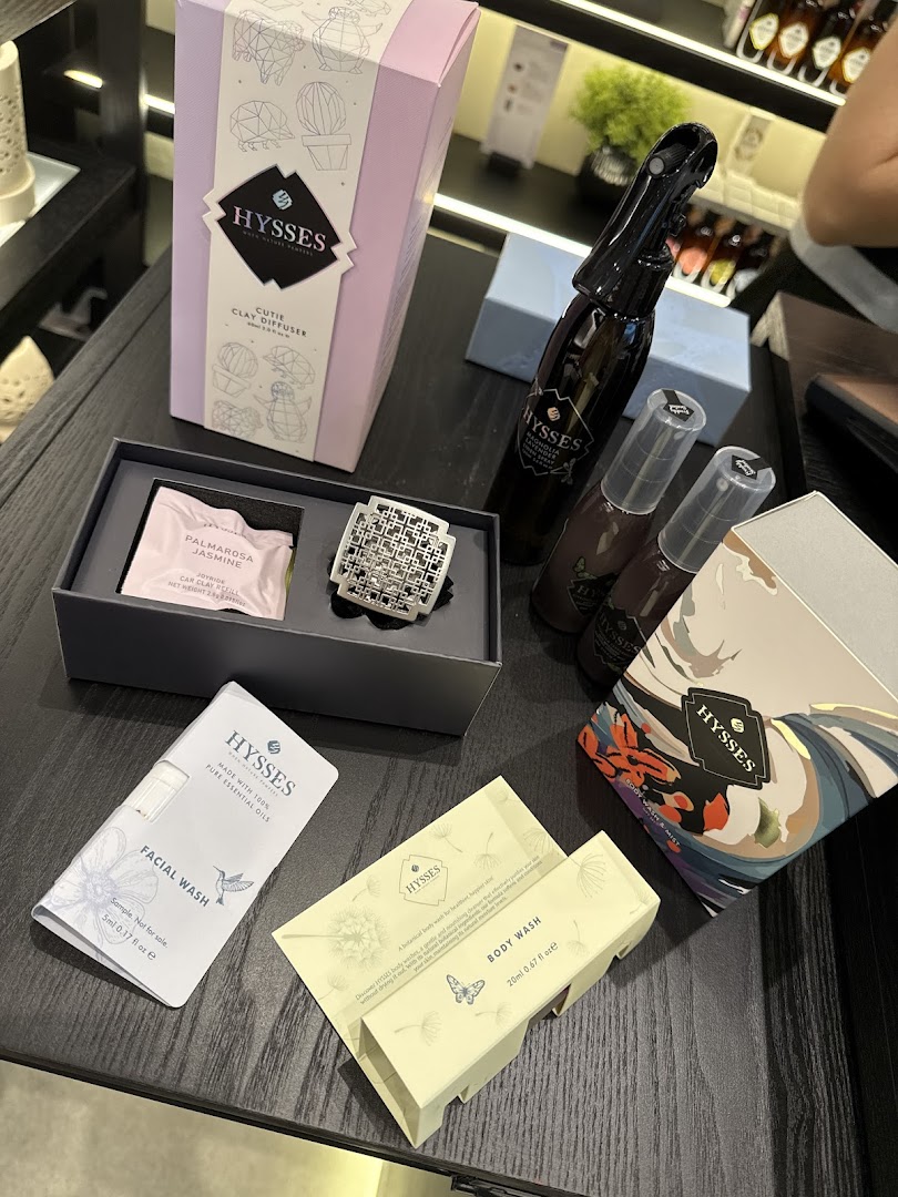 Various HYSSES home scents and personal care products displayed on a dark surface.