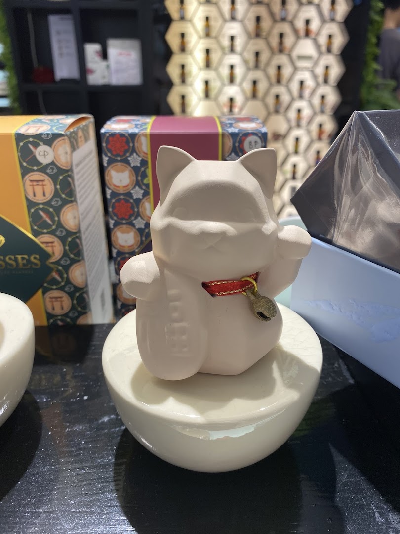Close-up of a decorative lucky cat figurine and product packaging in a home scents shop.