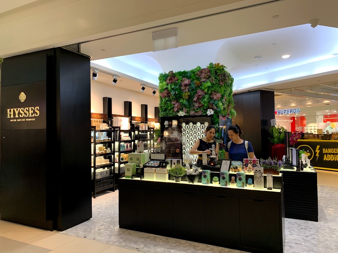 Two women interact with products inside the HYSSES shop, featuring home scents and wellness items.