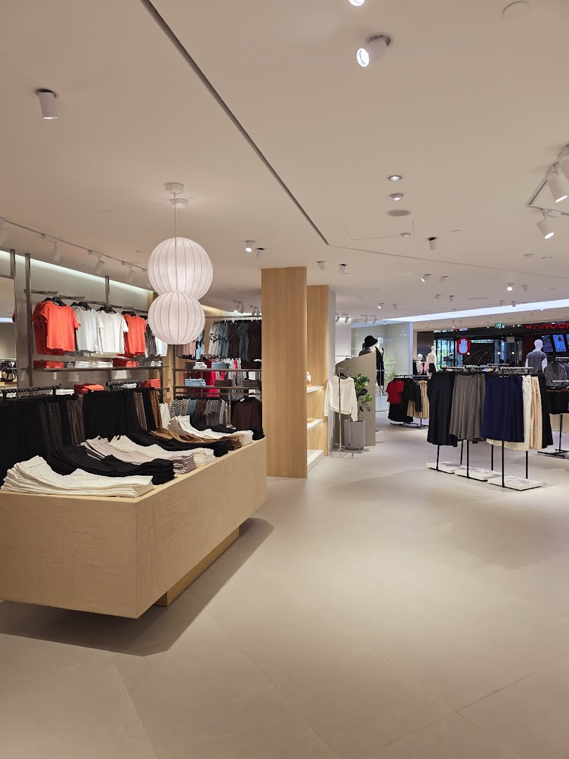 An interior view of a modern clothing store featuring neatly arranged apparel on racks and display tables.