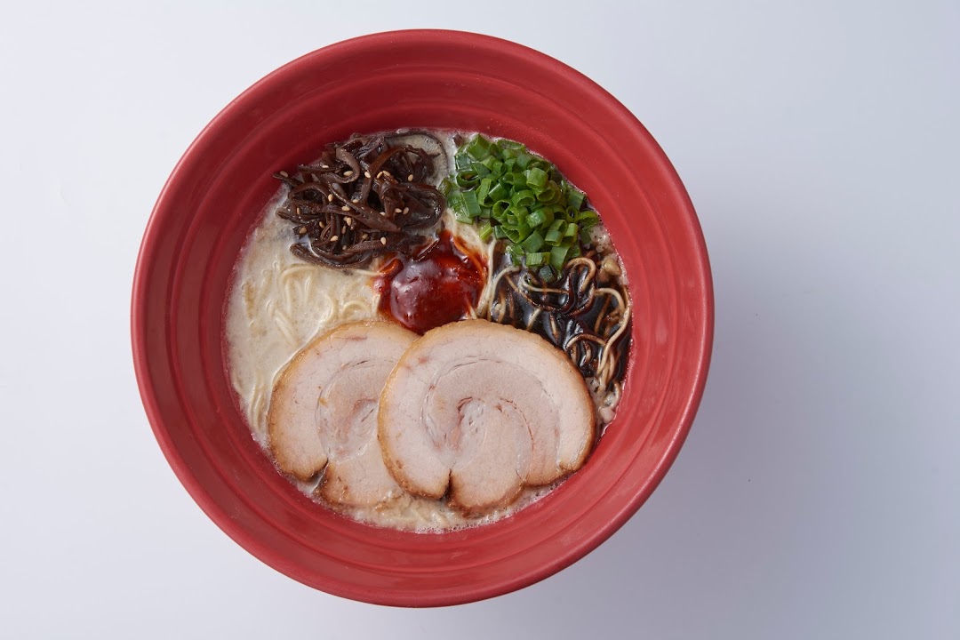 An overhead shot of a vibrant red bowl filled with delicious ramen, topped with chashu, scallions, and mushrooms.