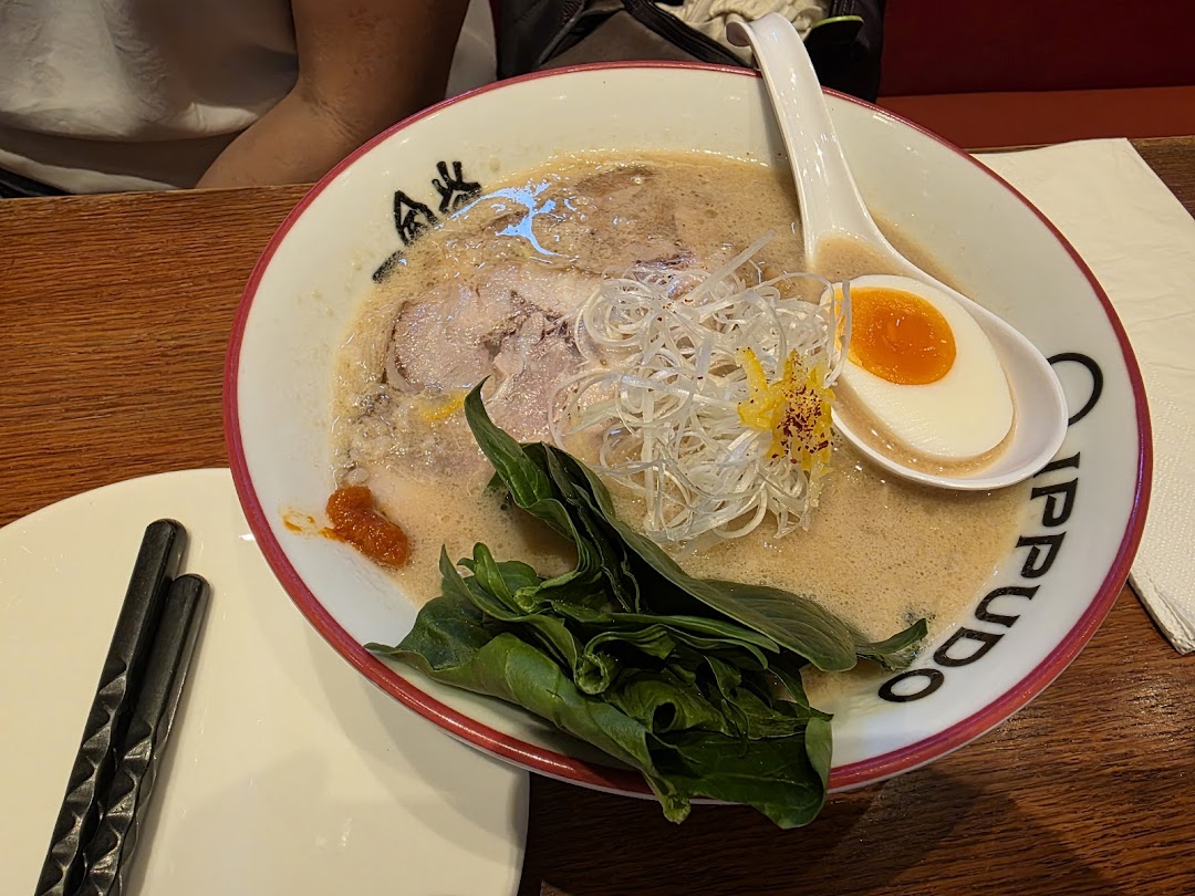 A close-up of a delicious bowl of ramen from IPPUDO, featuring pork, egg, and fresh greens.