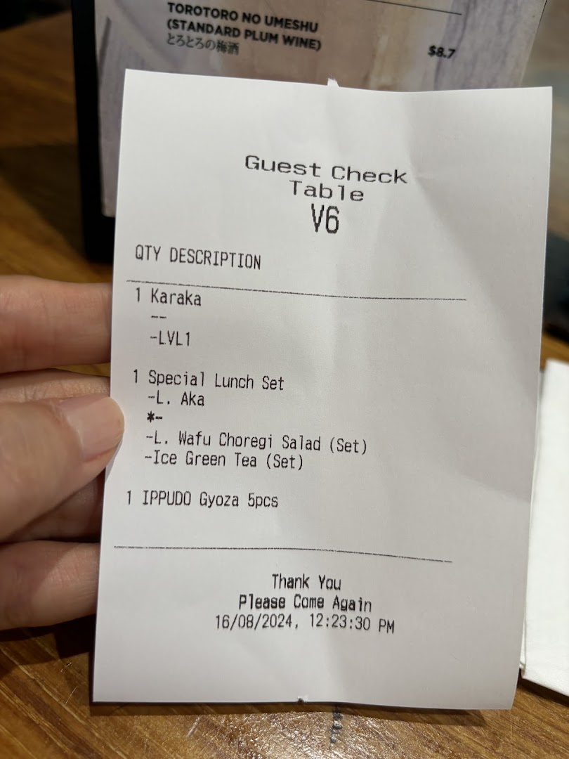 A hand holds a guest check from IPPUDO, detailing ordered items like ramen, a lunch set, and gyoza.