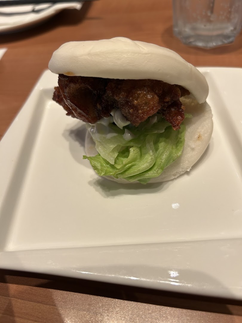 A delicious bao bun filled with crispy fried chicken, fresh lettuce, and creamy sauce on a white plate.
