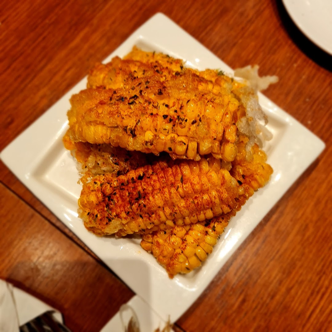 Close-up of seasoned corn on the cob pieces served on a white rectangular plate.