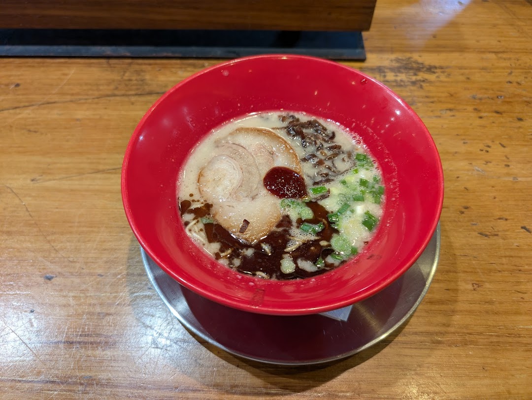 A vibrant red bowl of ramen with pork, scallions, and a rich broth on a wooden table.
