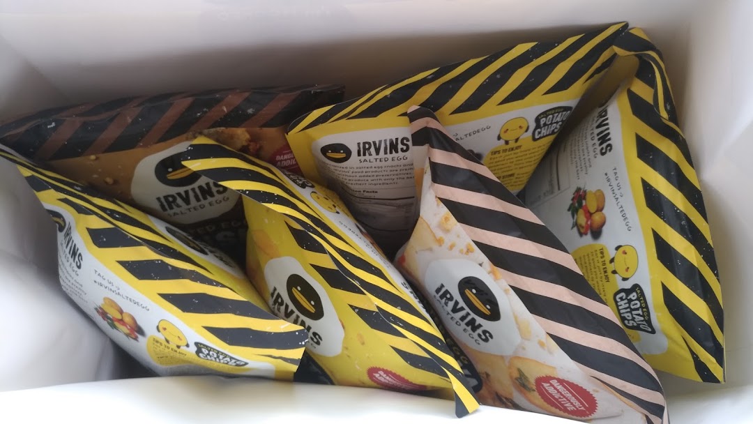 A close-up view of multiple Irvins Salted Egg snack bags inside a white shopping bag.
