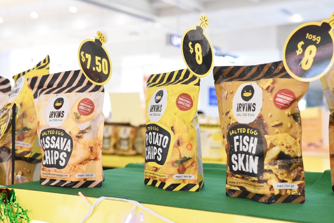 Close-up display of Irvins Salted Egg products, including Cassava Chips, Potato Chips, and Fish Skin, with prices.