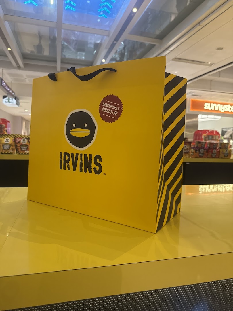 A bright yellow IRVINS shopping bag with its distinctive logo and 'Dangerously Addictive' slogan.