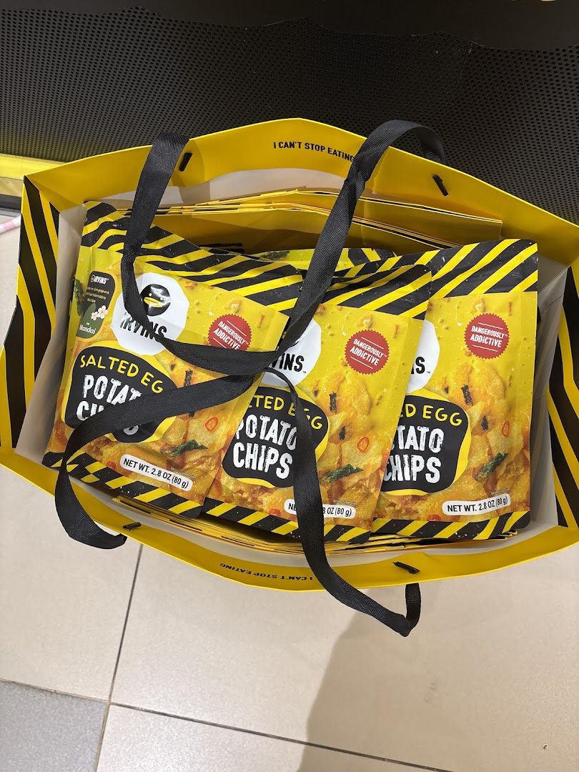 Several bags of IRVINS Salted Egg Potato Chips are seen inside a yellow shopping bag.