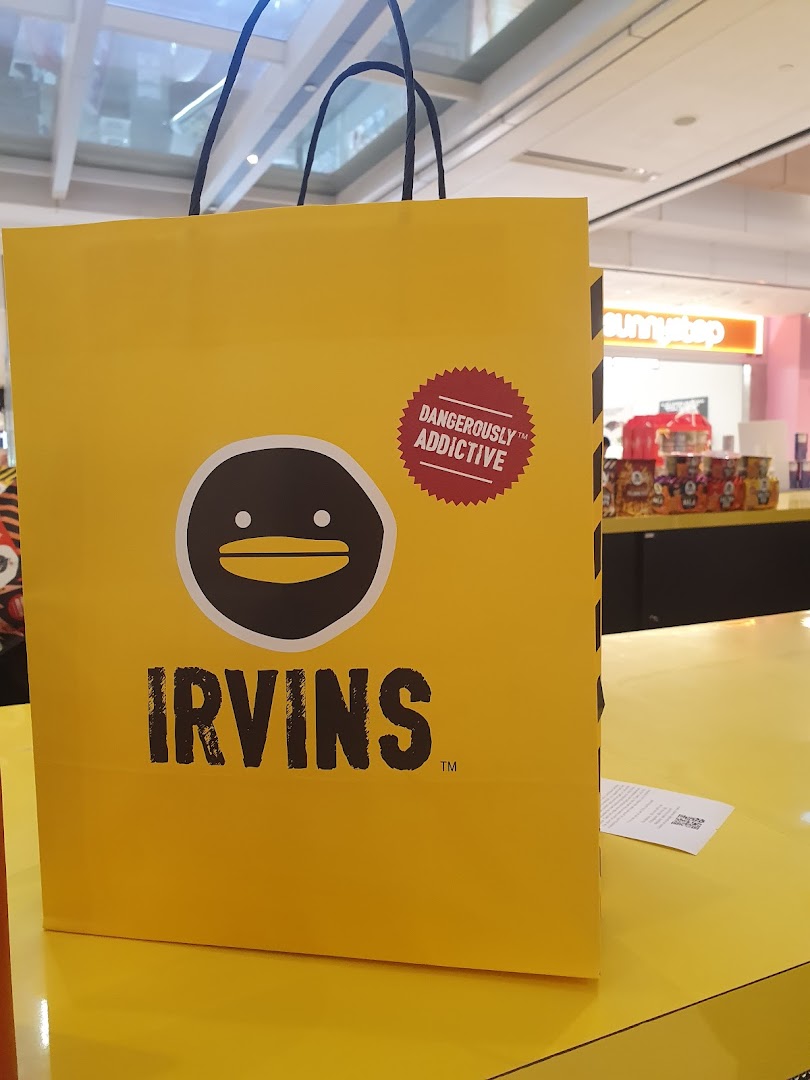 A bright yellow IRVINS shopping bag featuring its distinctive logo and 'Dangerously Addictive' slogan.