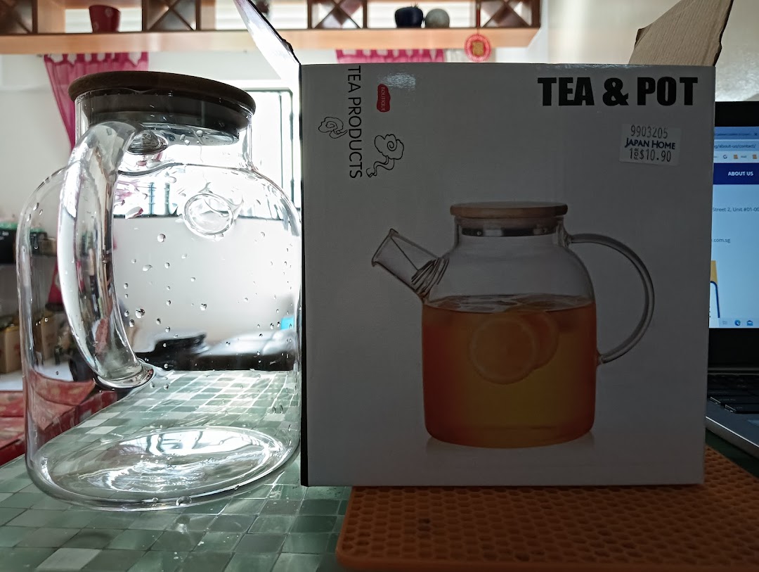 A clear glass pitcher stands next to its 'Tea & Pot' product packaging from Japan Home.
